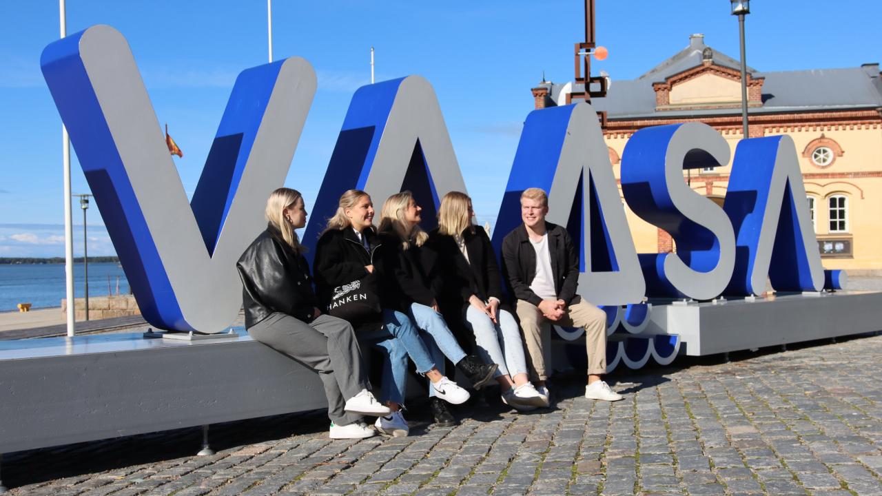 Students sitting outside in front of a sign saying "Vaasa"