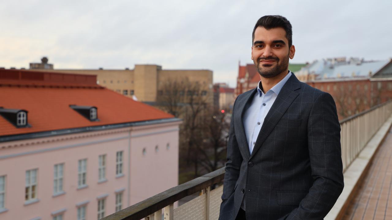 Mansoor Afzali står på en balkong och tittar in mot kameran, med hus i bakgrunden.