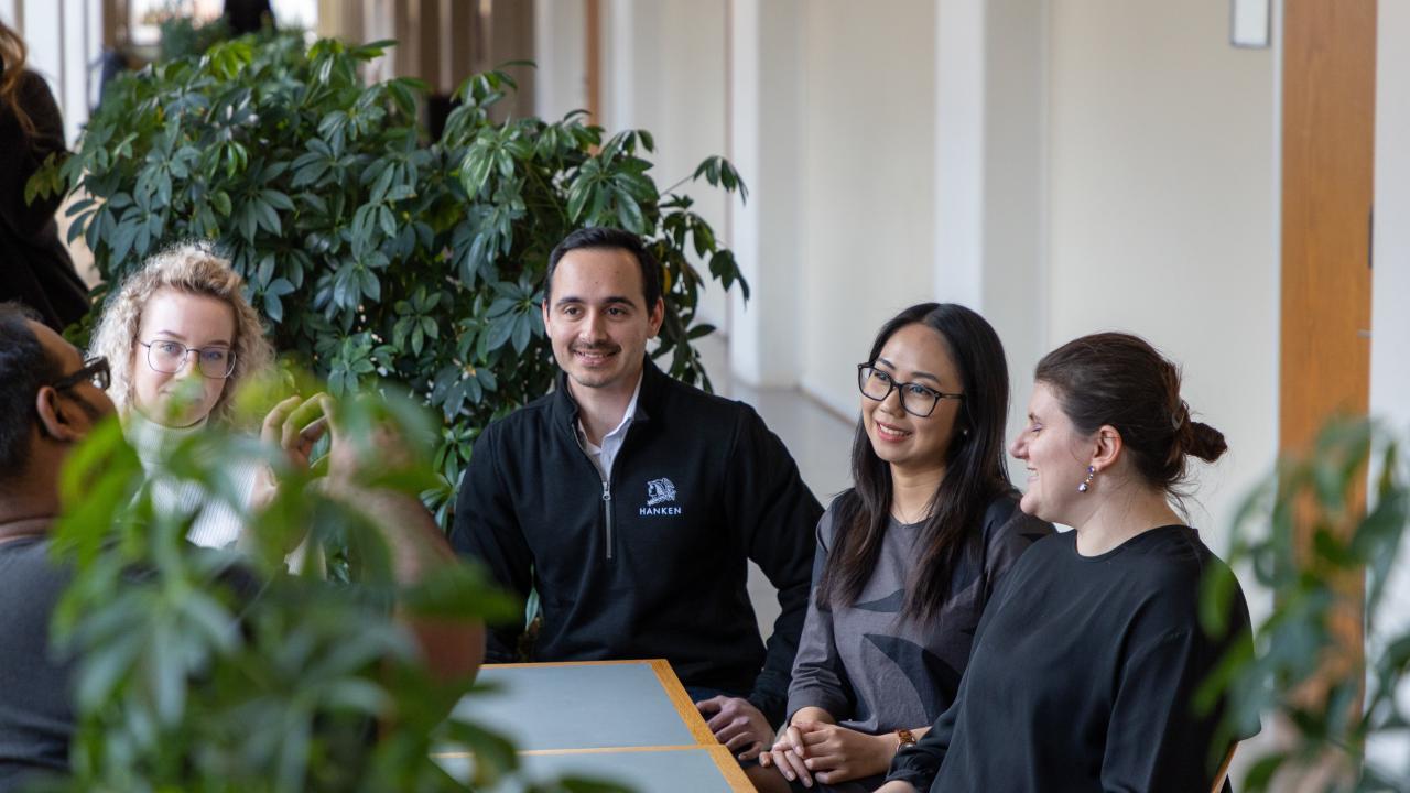 Five PhD students sitting at a table with plants in the background