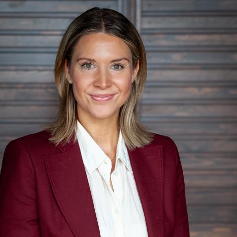 Kvinna med ljusbrunt hår till axlarna, vackert leende, vin röd blazer med vit kragskjorta